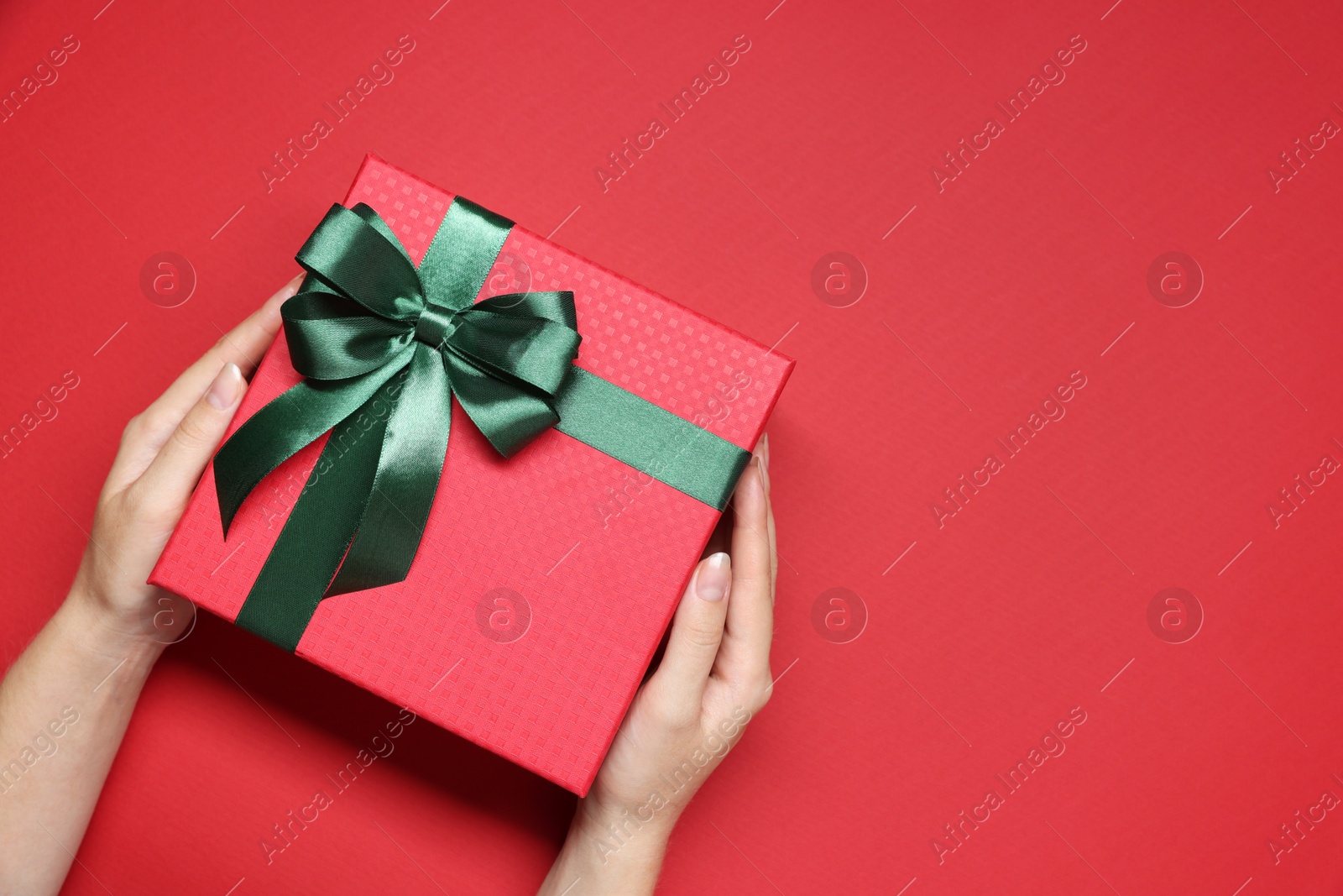 Photo of Woman holding gift box with bow on red background, top view. Space for text