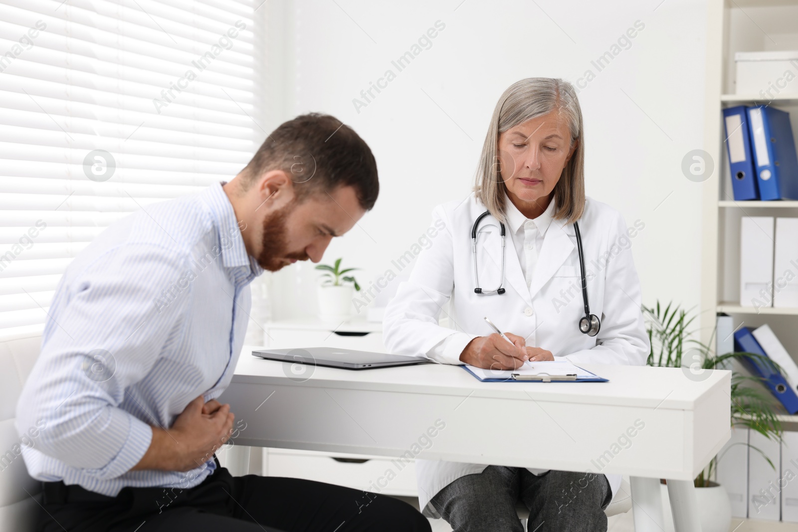 Photo of Doctor consulting patient with stomach pain at table in clinic