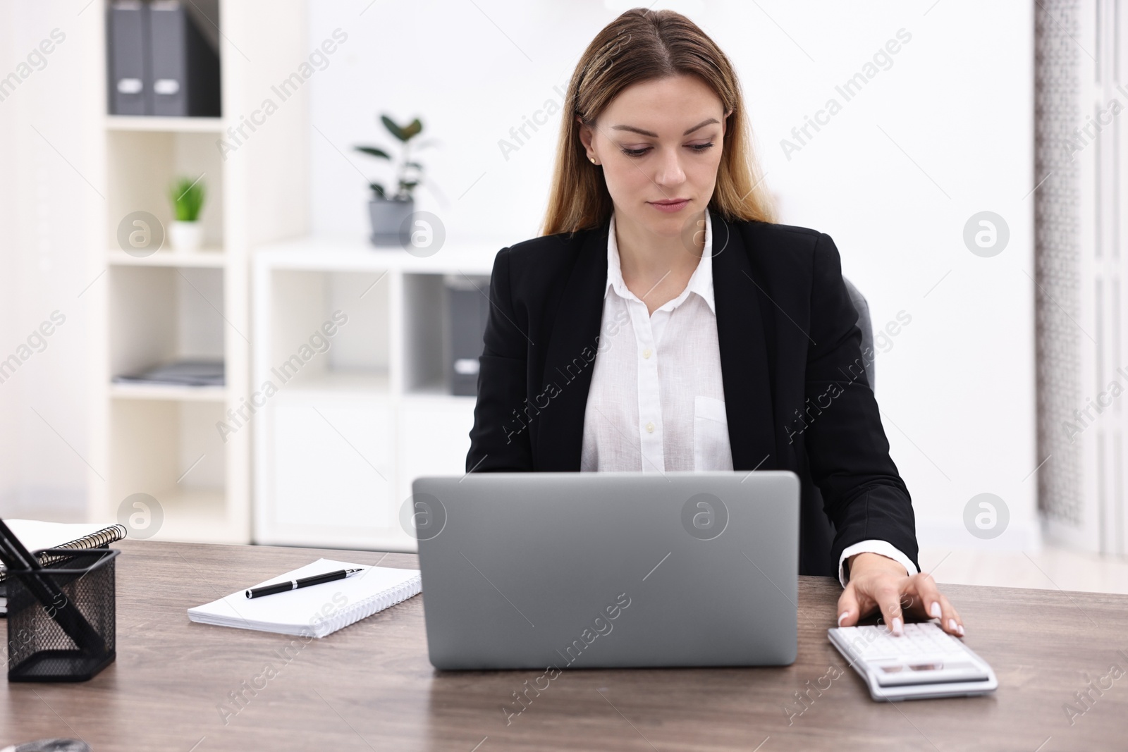 Photo of Banker with laptop and calculator working at wooden table in office