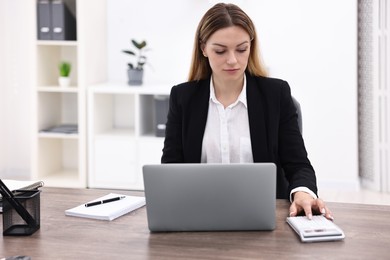 Photo of Banker with laptop and calculator working at wooden table in office