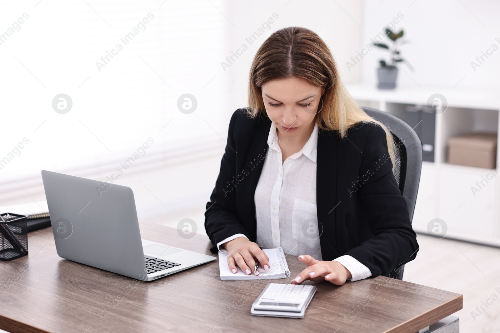 Photo of Banker with notebook using calculator at wooden table in office