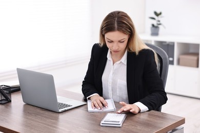 Photo of Banker with notebook using calculator at wooden table in office