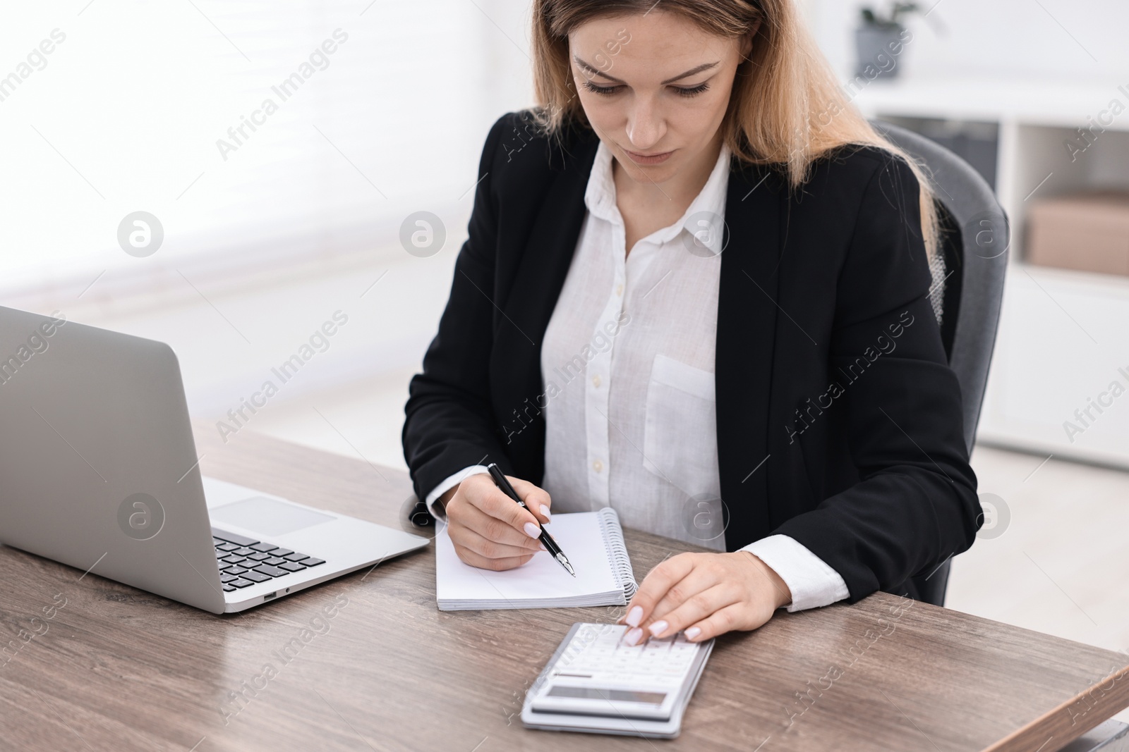 Photo of Banker with notebook using calculator at wooden table in office