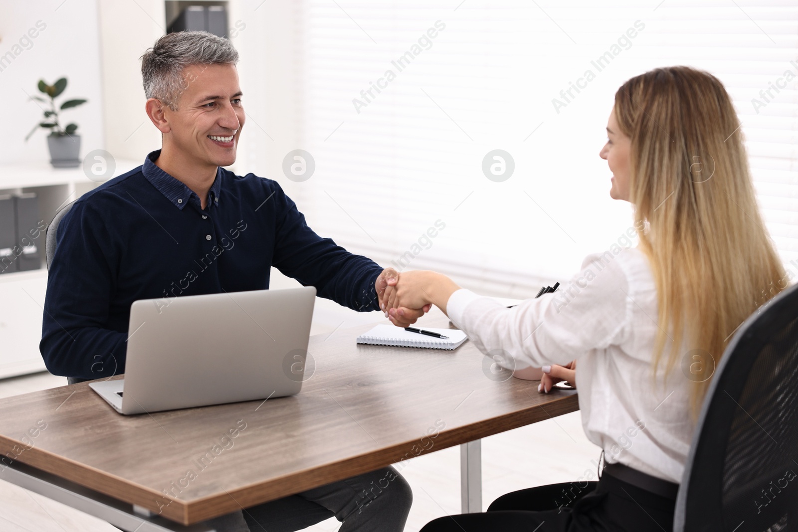 Photo of Banker and client shaking hands at table in office