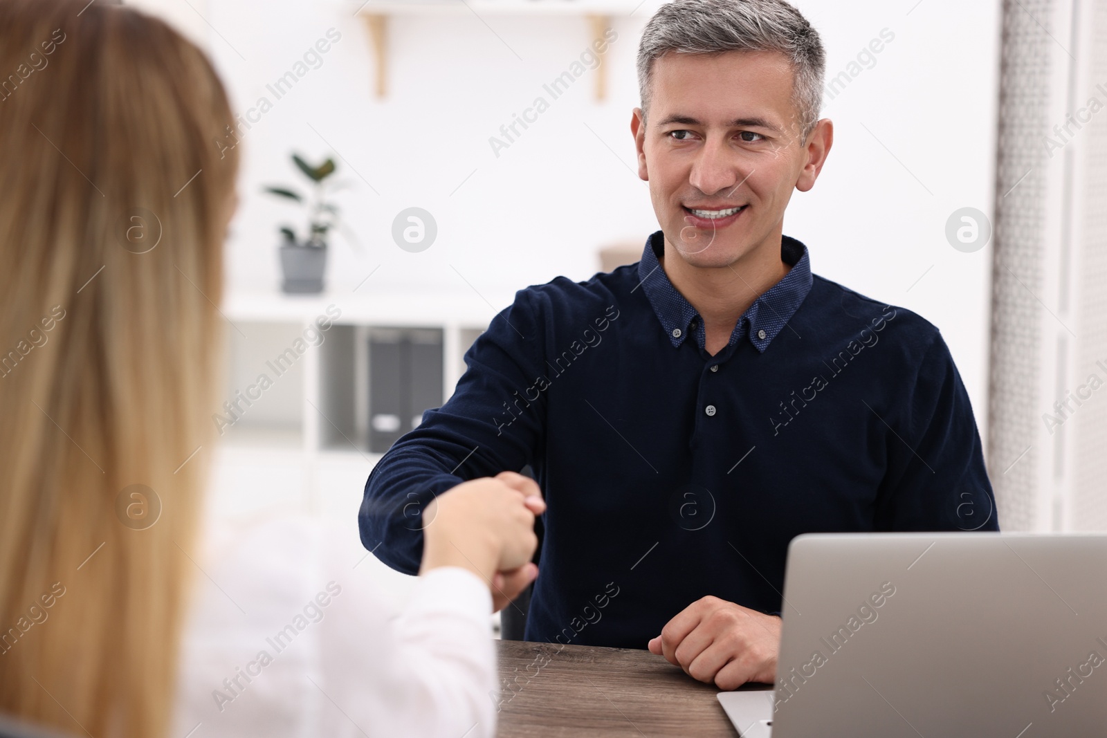 Photo of Banker and client shaking hands at table in office