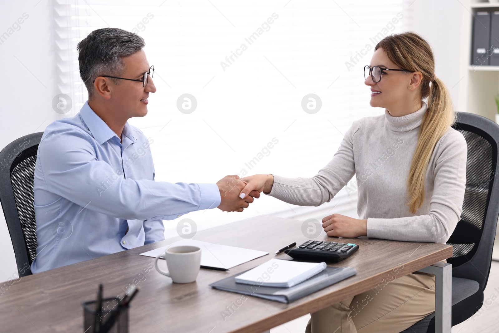 Photo of Banker and client shaking hands at table in office