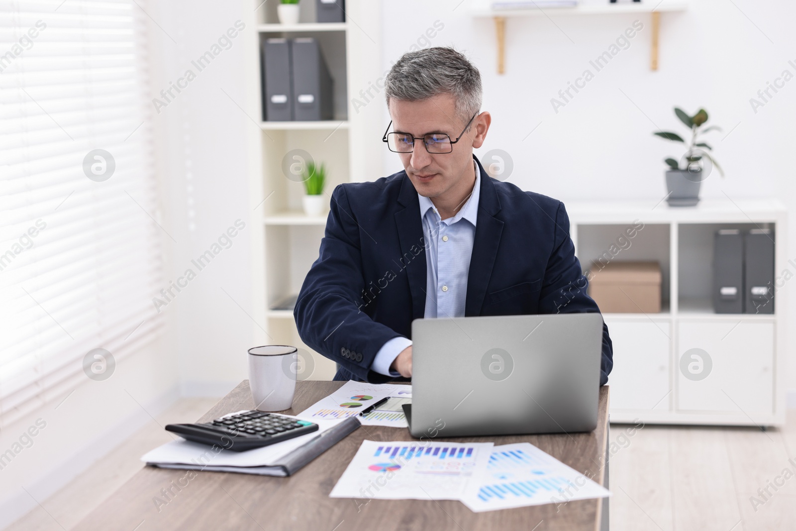 Photo of Banker with laptop working at wooden table in office