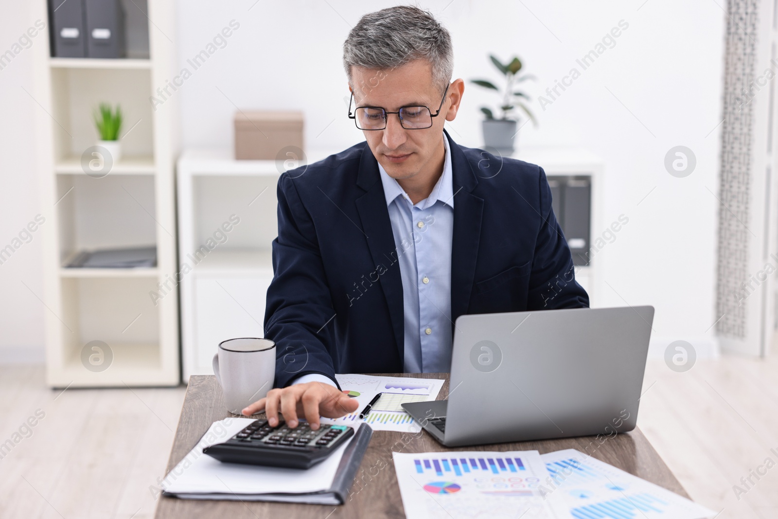 Photo of Banker with laptop and calculator working at wooden table in office