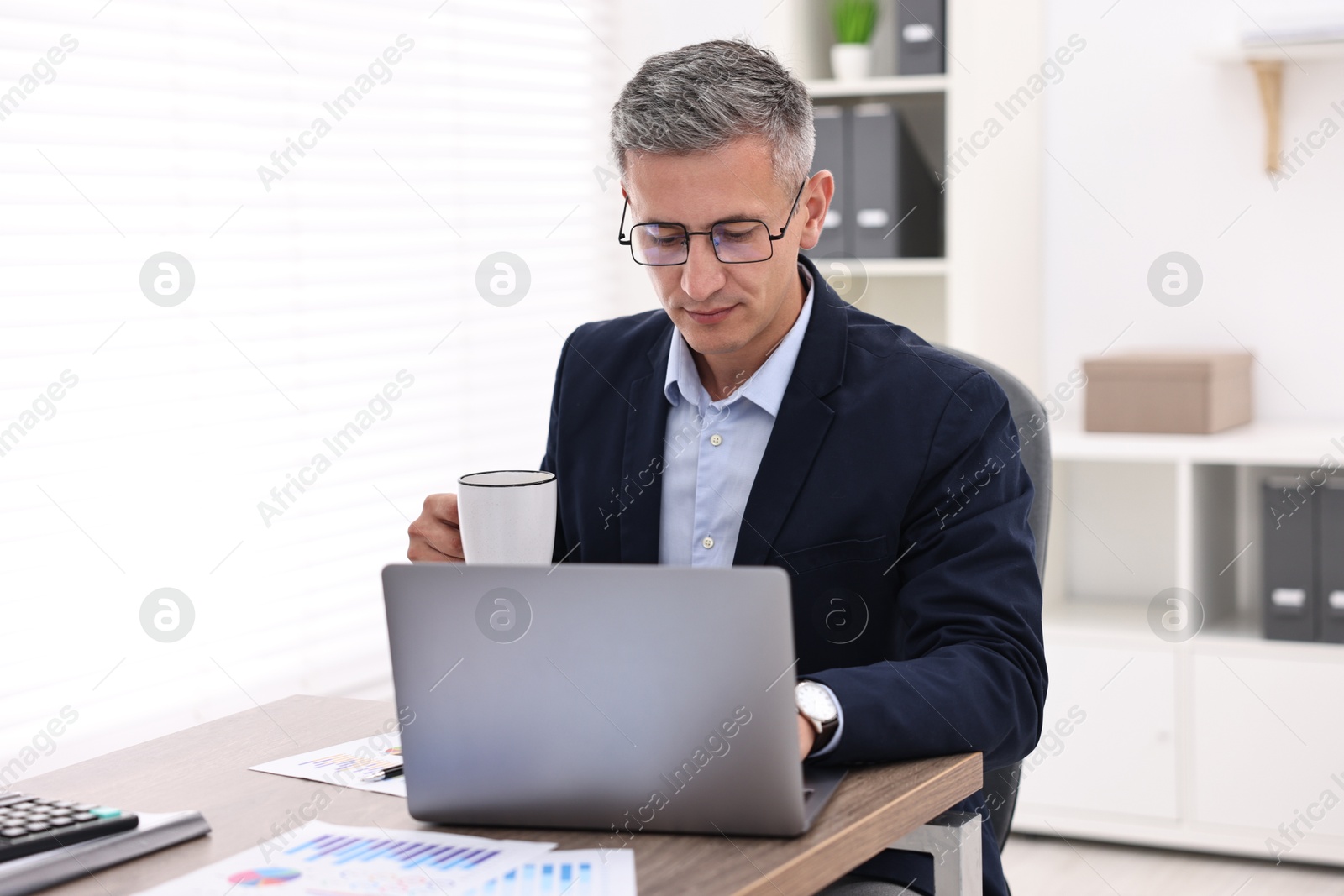 Photo of Banker with cup and laptop at wooden table in office