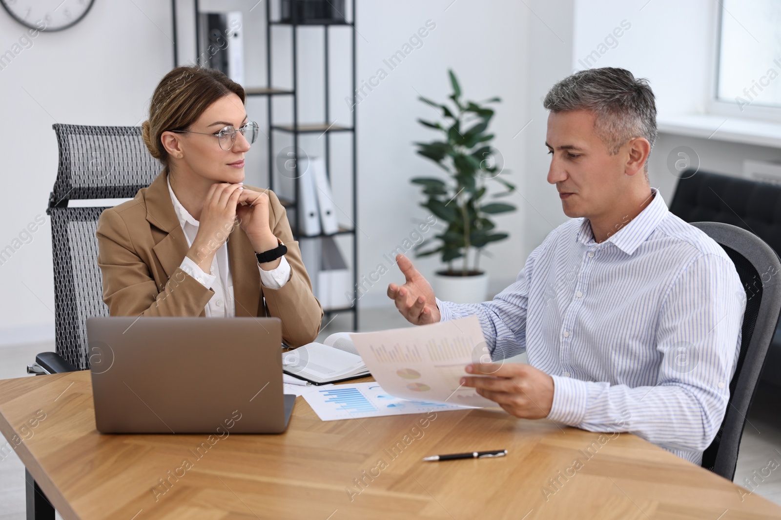 Photo of Banker working with client at wooden table in office