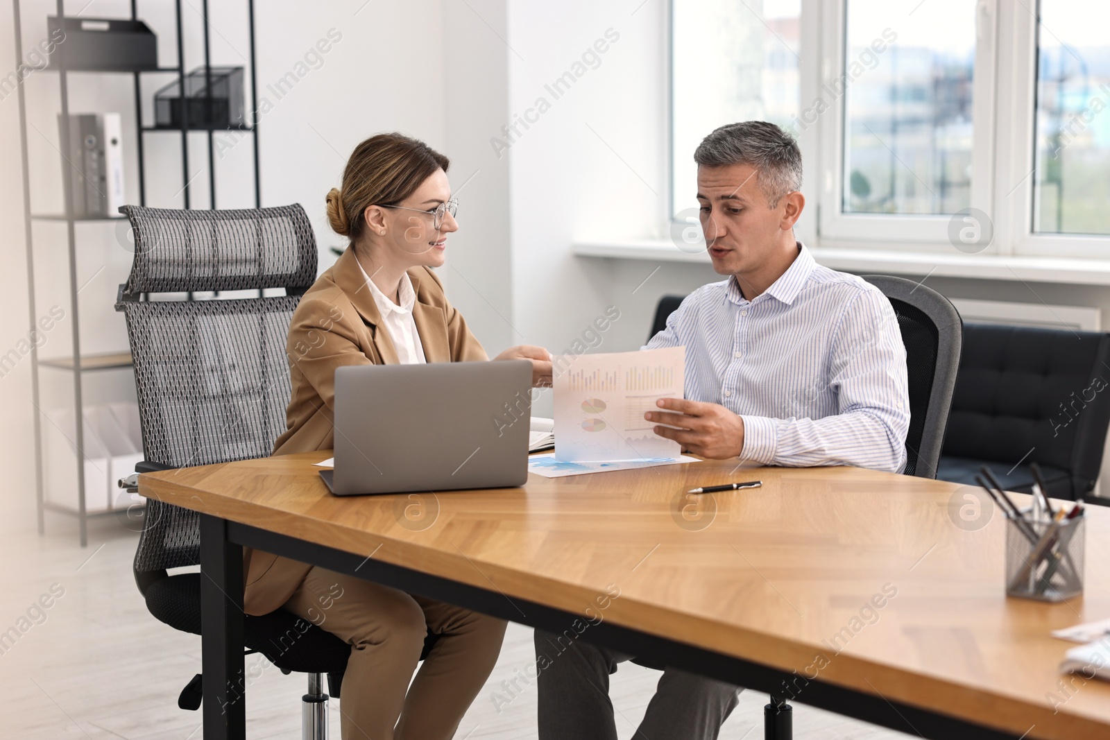 Photo of Banker working with client at wooden table in office