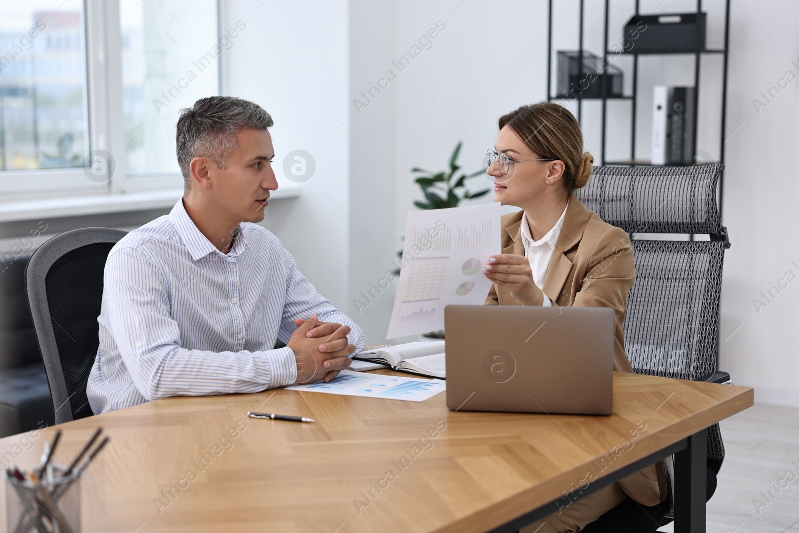 Photo of Banker working with client at wooden table in office