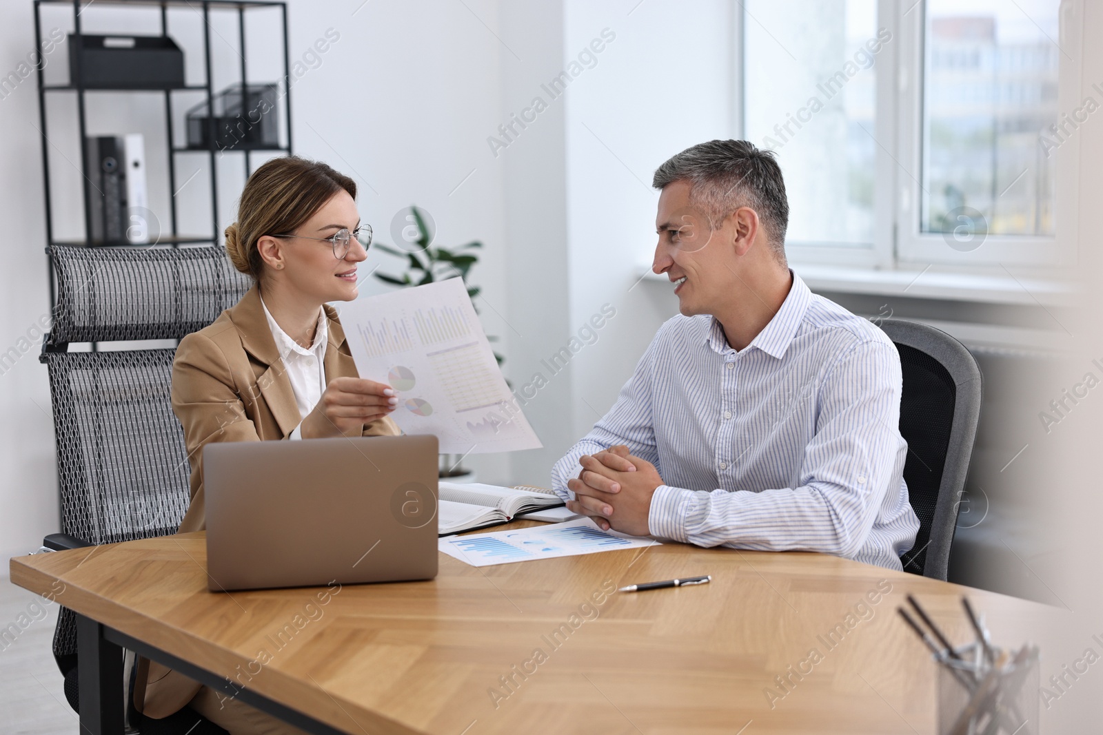 Photo of Banker working with client at wooden table in office