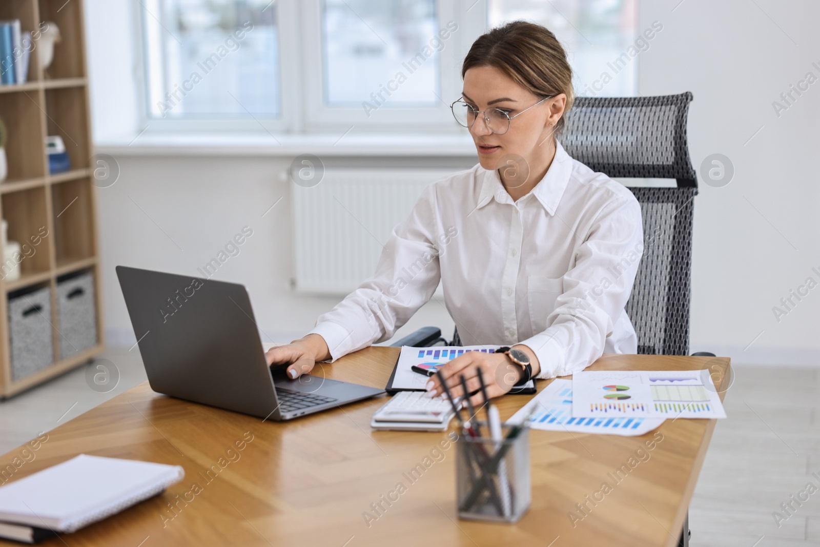 Photo of Banker with laptop and calculator working at wooden table in office