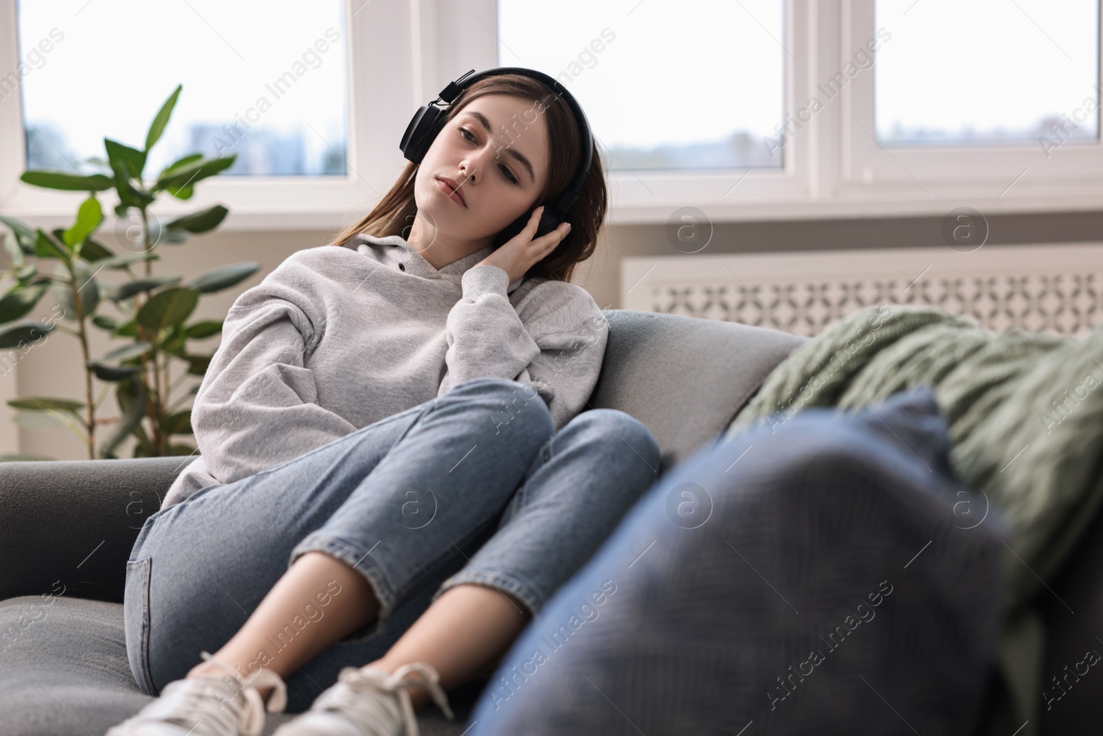 Photo of Loneliness concept. Sad teenage girl in headphones listening to music on sofa at home