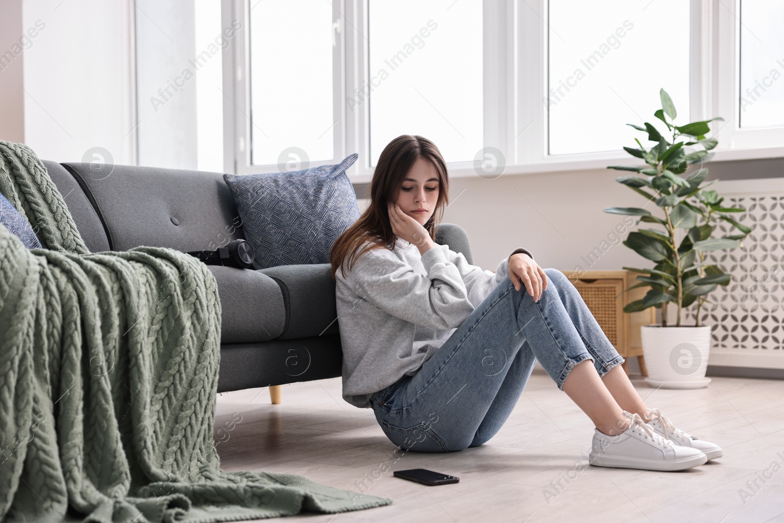 Photo of Loneliness concept. Sad teenage girl with smartphone on floor at home