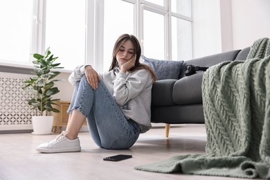 Loneliness concept. Sad teenage girl with smartphone on floor at home