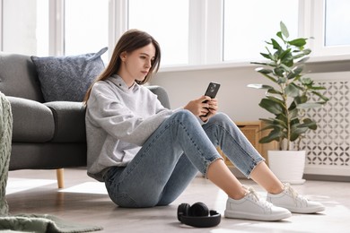 Loneliness concept. Sad teenage girl using smartphone on floor at home