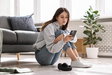 Photo of Loneliness concept. Sad teenage girl using smartphone on floor at home