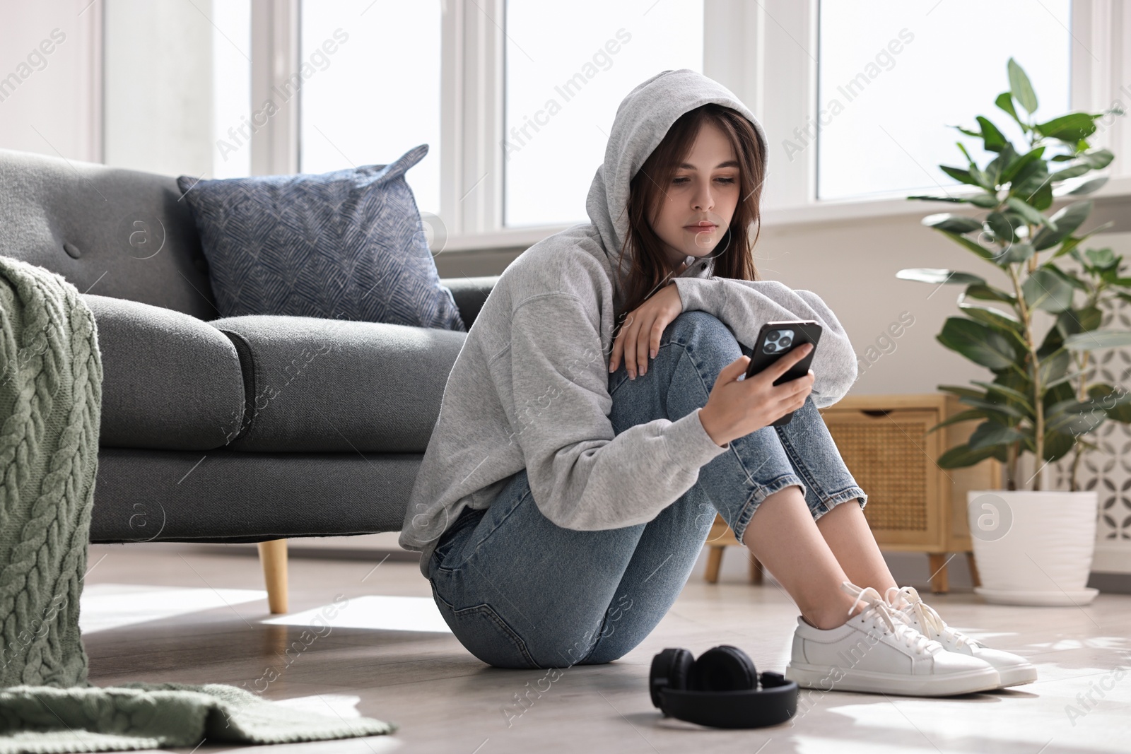 Photo of Loneliness concept. Sad teenage girl using smartphone on floor at home