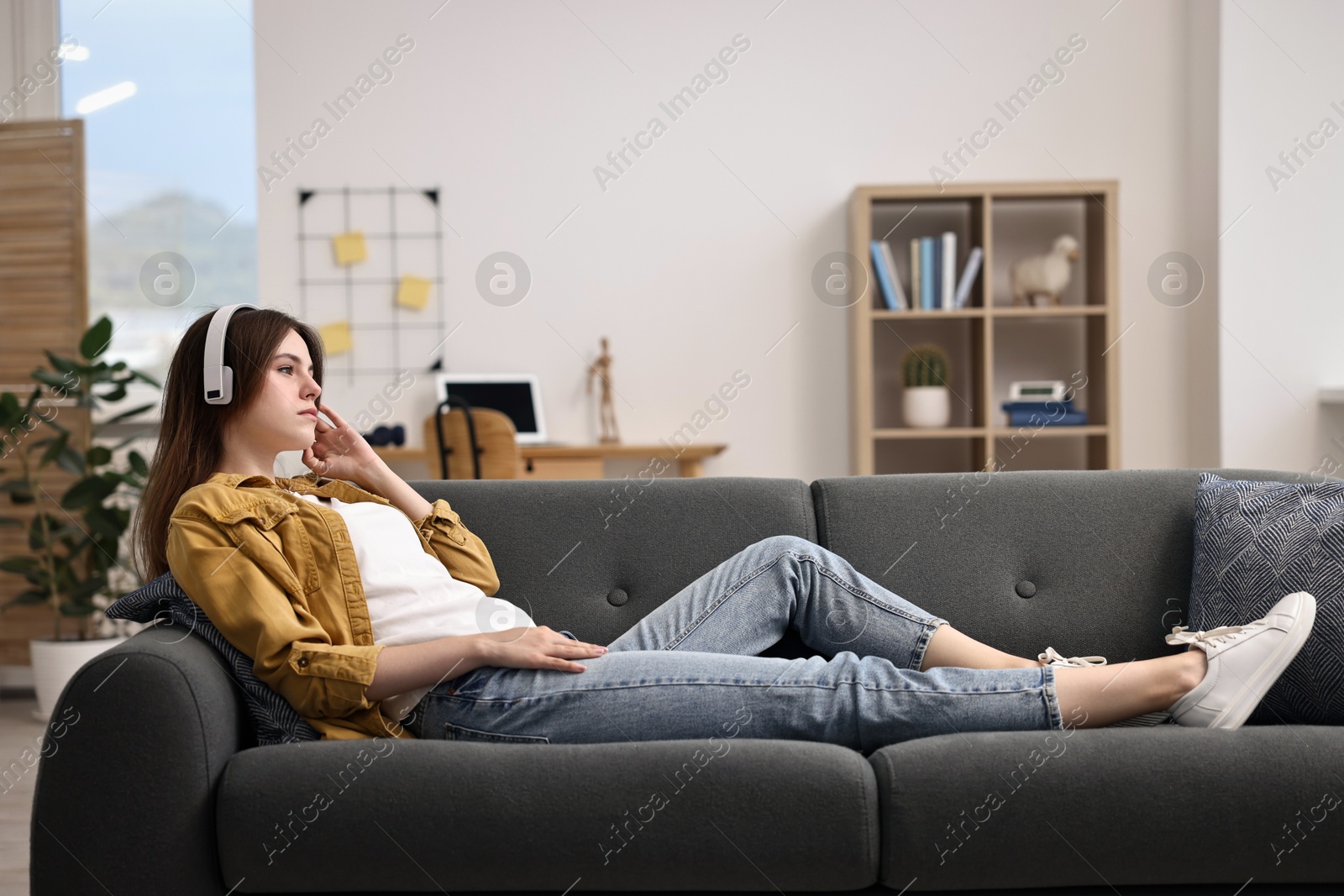 Photo of Loneliness concept. Sad teenage girl in headphones listening to music on sofa at home