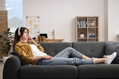 Loneliness concept. Sad teenage girl in headphones listening to music on sofa at home