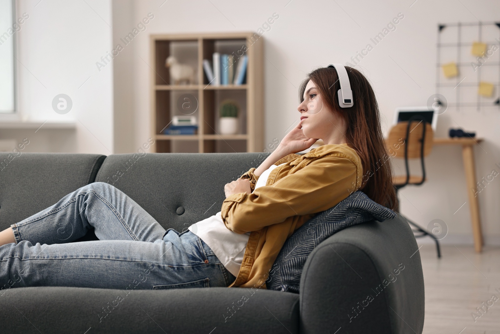 Photo of Loneliness concept. Sad teenage girl in headphones listening to music on sofa at home