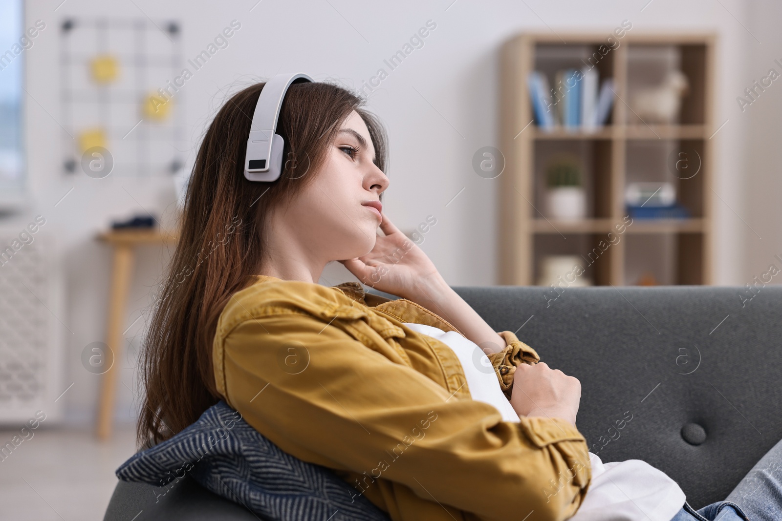 Photo of Loneliness concept. Sad teenage girl in headphones listening to music on sofa at home