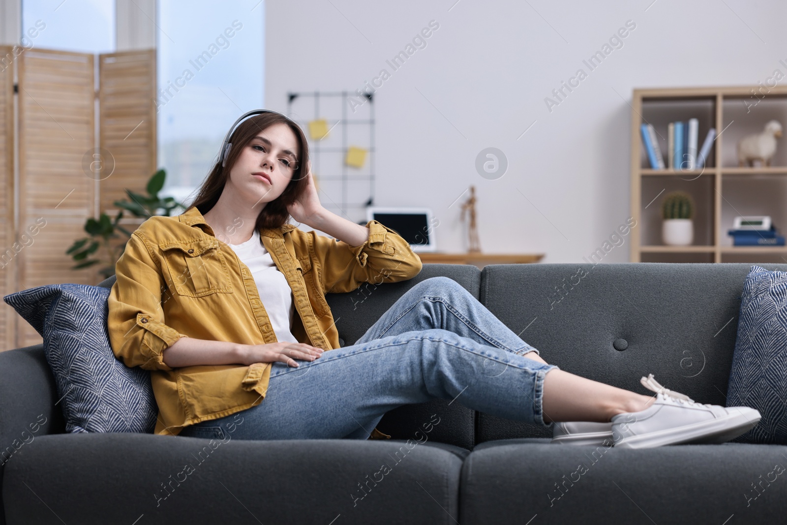 Photo of Loneliness concept. Sad teenage girl in headphones listening to music on sofa at home