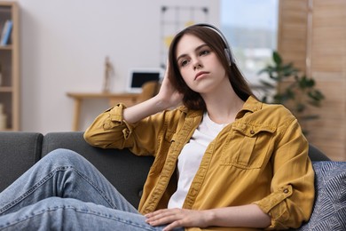 Loneliness concept. Sad teenage girl in headphones listening to music on sofa at home