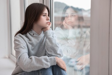 Photo of Loneliness concept. Sad teenage girl near window at home