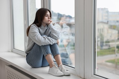 Loneliness concept. Sad teenage girl on windowsill at home