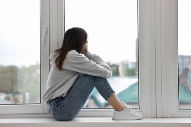 Photo of Loneliness concept. Sad teenage girl on windowsill at home