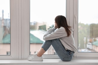 Loneliness concept. Sad teenage girl on windowsill at home