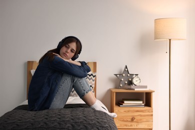 Loneliness concept. Sad teenage girl in headphones listening to music on bed at home