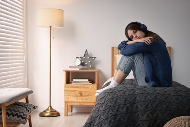 Photo of Loneliness concept. Sad teenage girl in headphones listening to music on bed at home