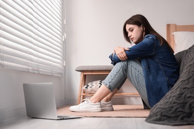 Loneliness concept. Sad teenage girl with laptop on floor at home