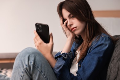 Loneliness concept. Sad teenage girl with smartphone at home