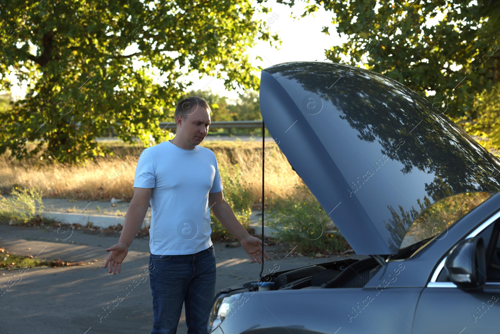 Photo of Stressed man looking under hood of broken car outdoors