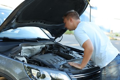 Photo of Stressed man looking under hood of broken car outdoors