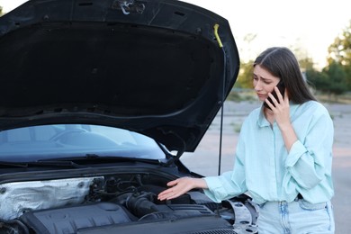 Stressed woman talking on phone near broken car outdoors