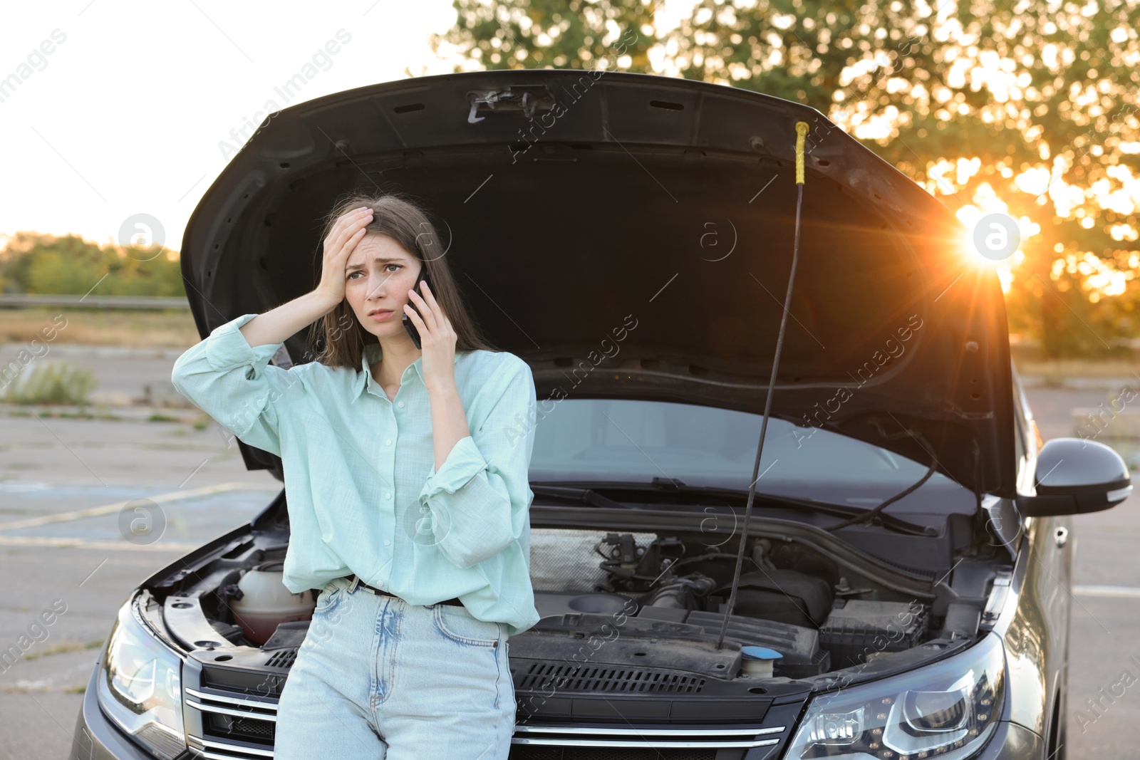 Photo of Stressed woman talking on phone near broken car outdoors