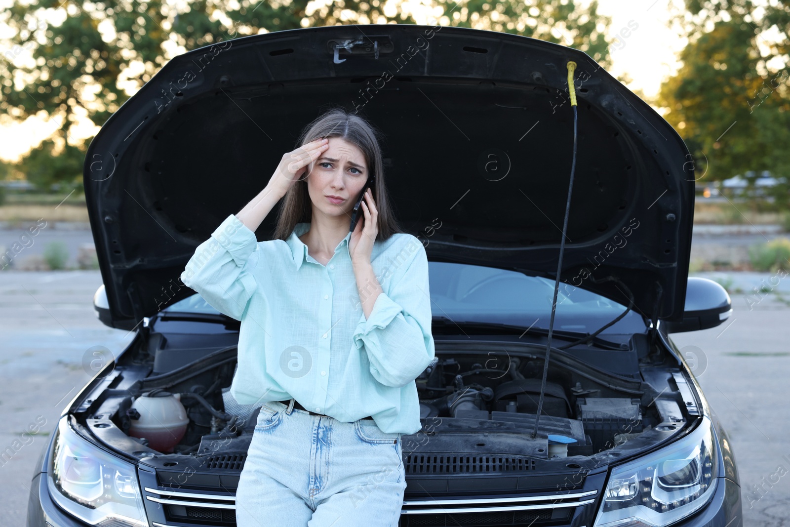 Photo of Stressed woman talking on phone near broken car outdoors