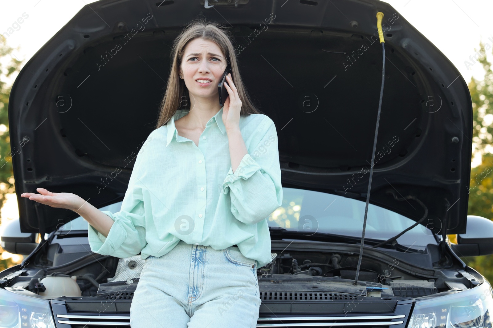 Photo of Stressed woman talking on phone near broken car outdoors