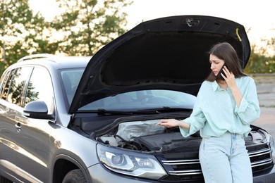 Photo of Stressed woman talking on phone near broken car outdoors