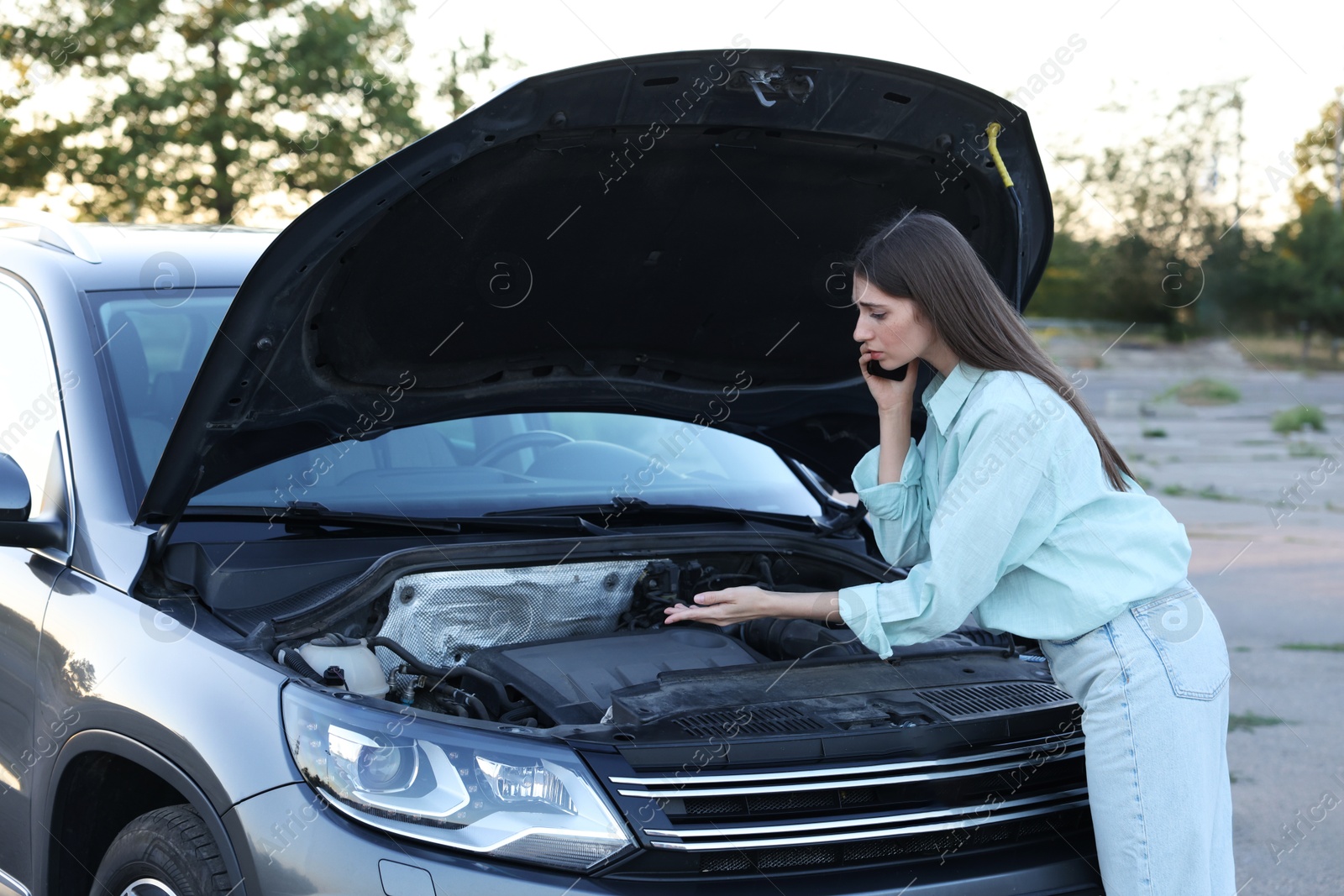 Photo of Stressed woman talking on phone near broken car outdoors