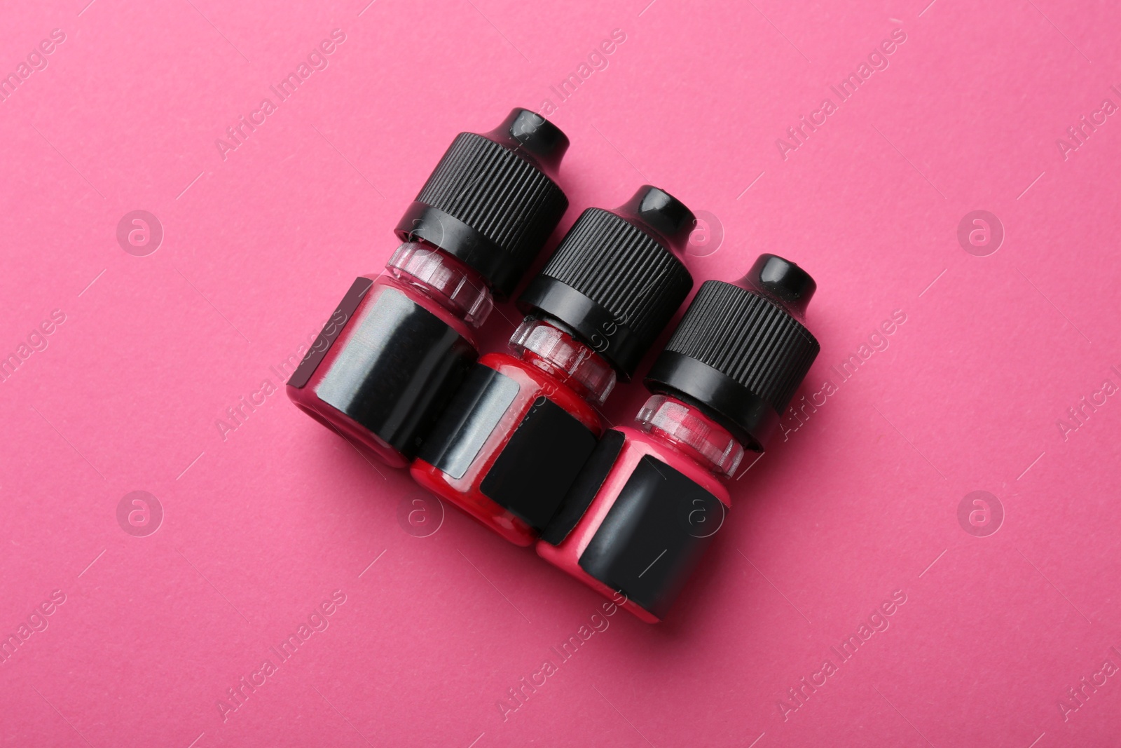 Photo of Bottles of pigments for permanent makeup on pink background, top view