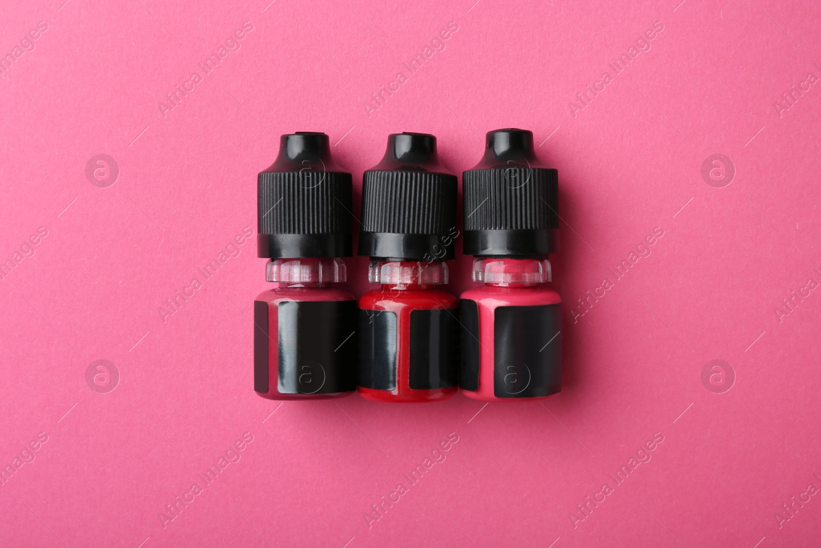 Photo of Bottles of pigments for permanent makeup on pink background, top view