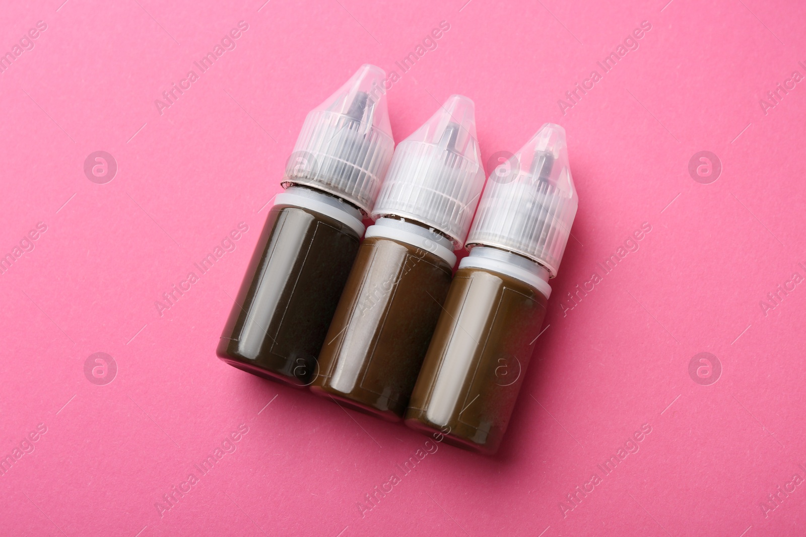 Photo of Bottles of pigments for permanent makeup on pink background, top view