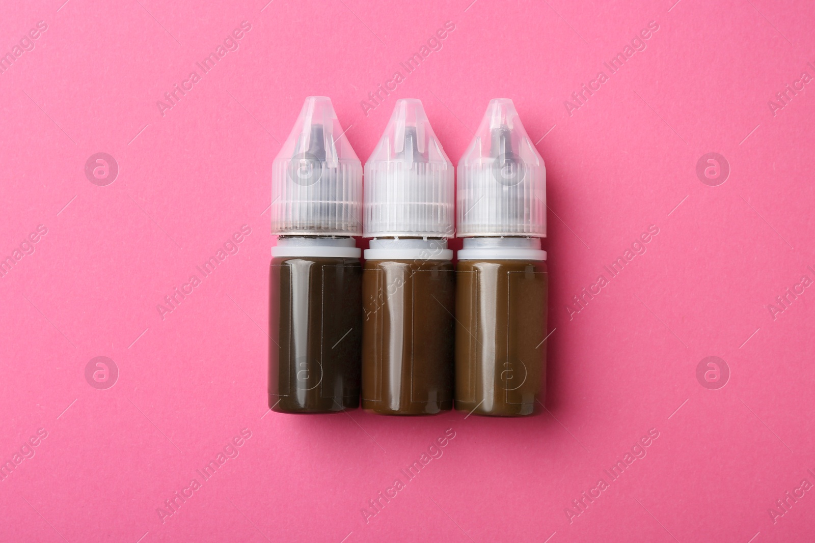 Photo of Bottles of pigments for permanent makeup on pink background, top view